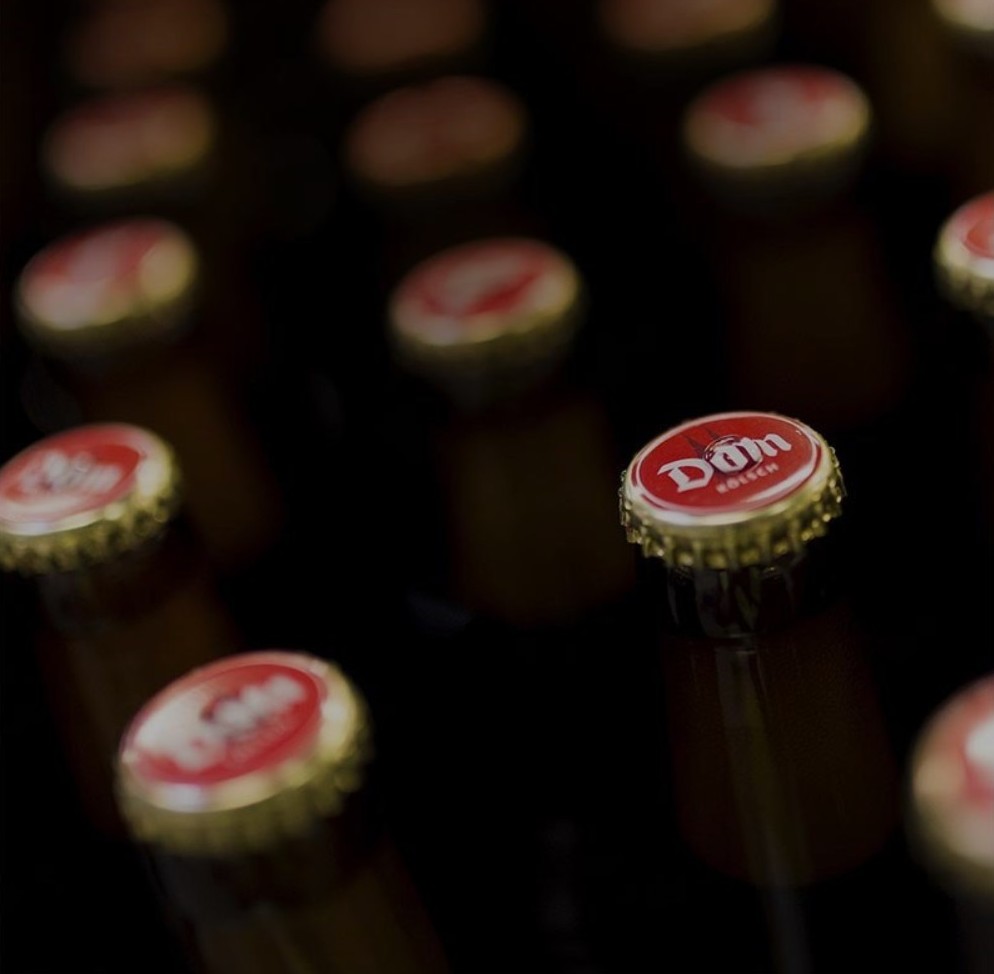 Eine Bierflasche steht im Fokus, hinter ihr sind viele unscharfe Flaschendeckel.